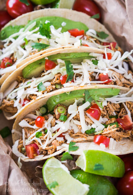 Three shredded chicken tacos garnished with tomato, avocado, and cilantro.