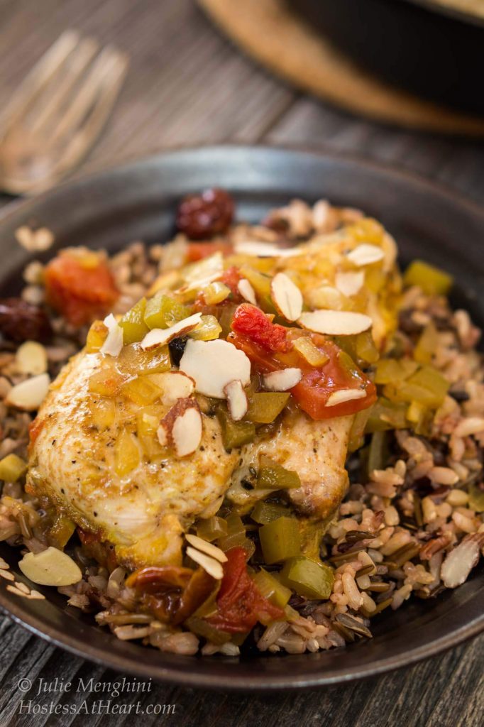 A bowl of filled with Indian flavored Chicken breast over a bed of rice topped with stewed tomatoes, green peppers, and sliced almonds.