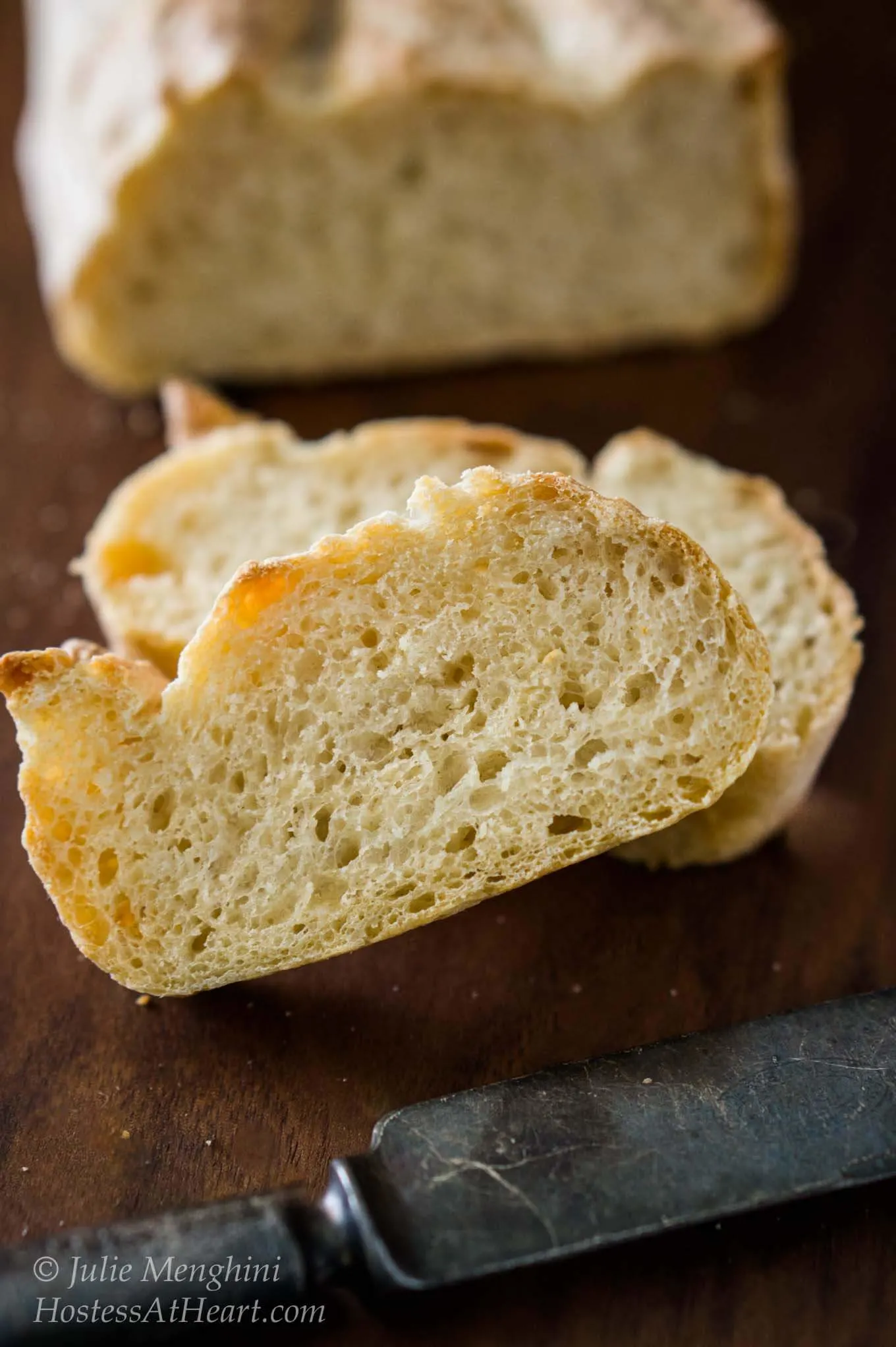 Two slices of Garlic Batard bread sitting in front of the loaf over a wooden cutting board.