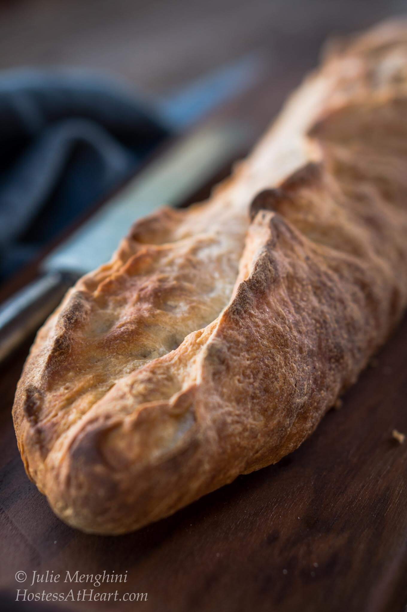 Front-view of a loaf of a Garlic Batard sitting on a wooding cutting board. A blue napkin sits in the background.
