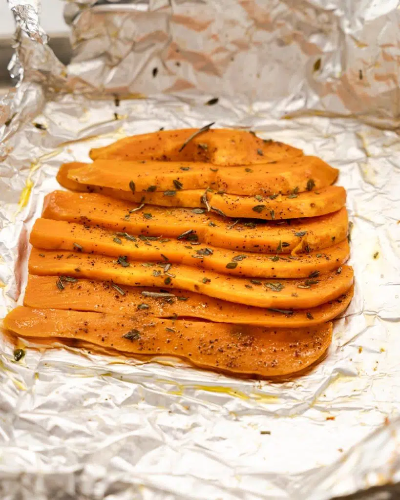 Sliced potatoes sitting on a piece of foil drizzled with olive oil and herbs