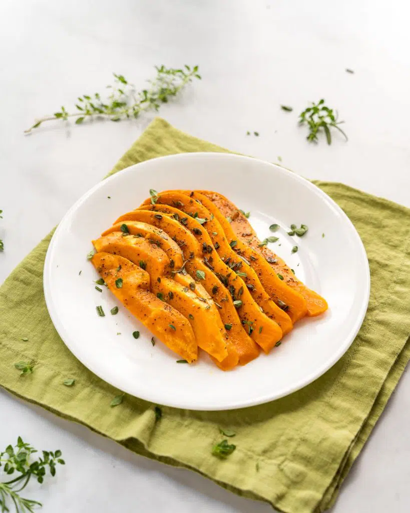 Cooked Sweet potato slices on a plate garnished with fresh herbs.