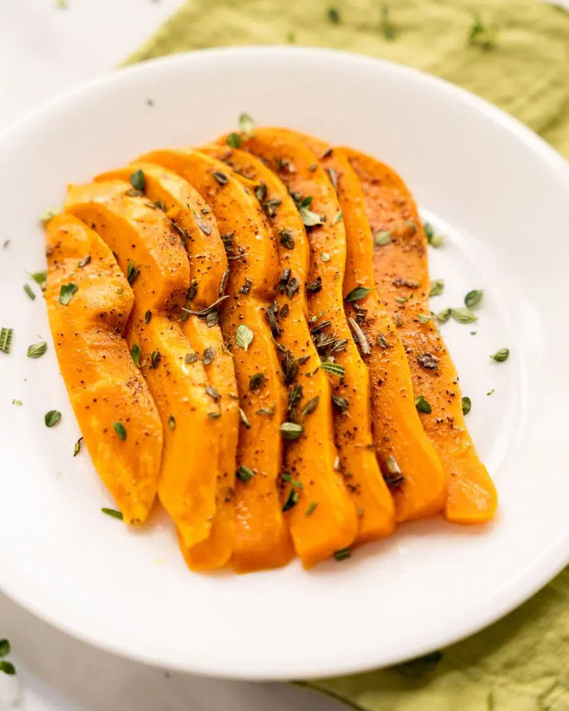 3/4 angle of sliced and fanned out sweet potatoes on a white plate.