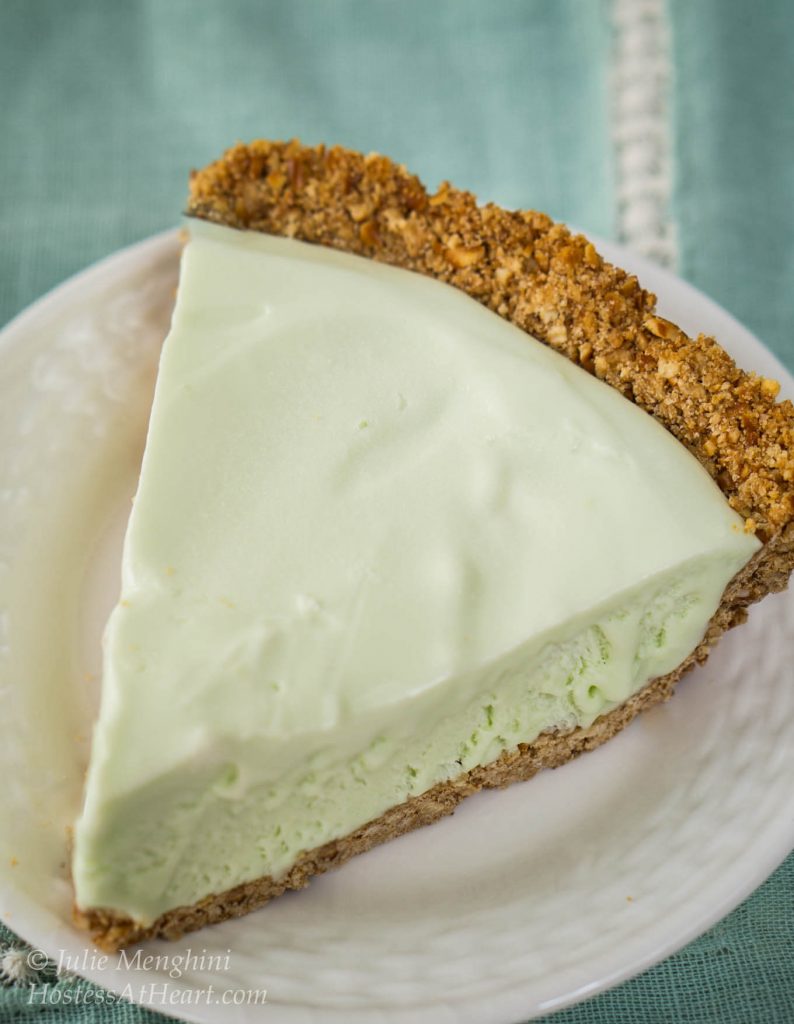Slice of green margarita pie with a graham cracker crust sitting on a white plate.