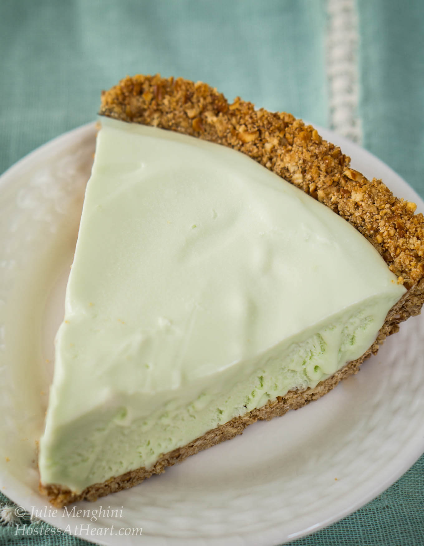 Slice of green margarita pie with a graham cracker crust sitting on a white plate.