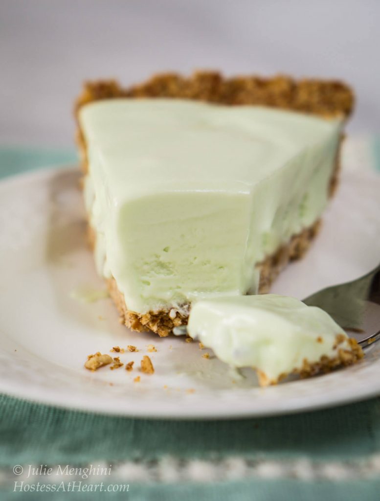 Table view of a slice of margarita pie. A fork has sliced off the front of the slice and lies beside it on a white plate.