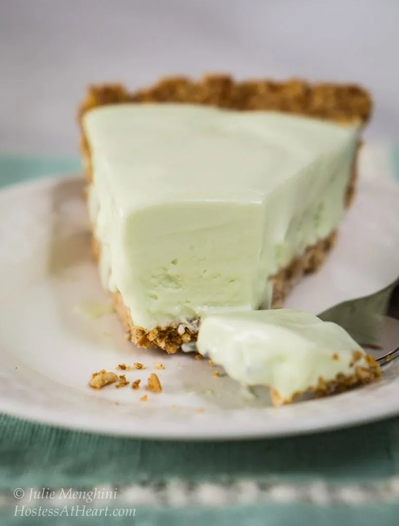 Table view of a slice of margarita pie. A fork has sliced off the front of the slice and lies beside it on a white plate.