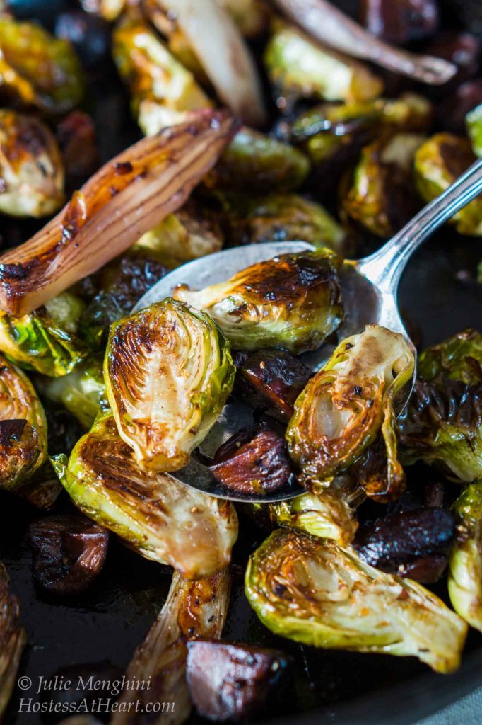 Top-down view of roasted brussels sprouts sitting on a serving spoon hovering over roasted Brussels sprouts with shallots and mushrooms.