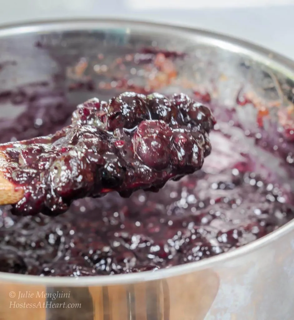 A wooden spoon filled with blueberry pineapple filling in a silver sauce pan.