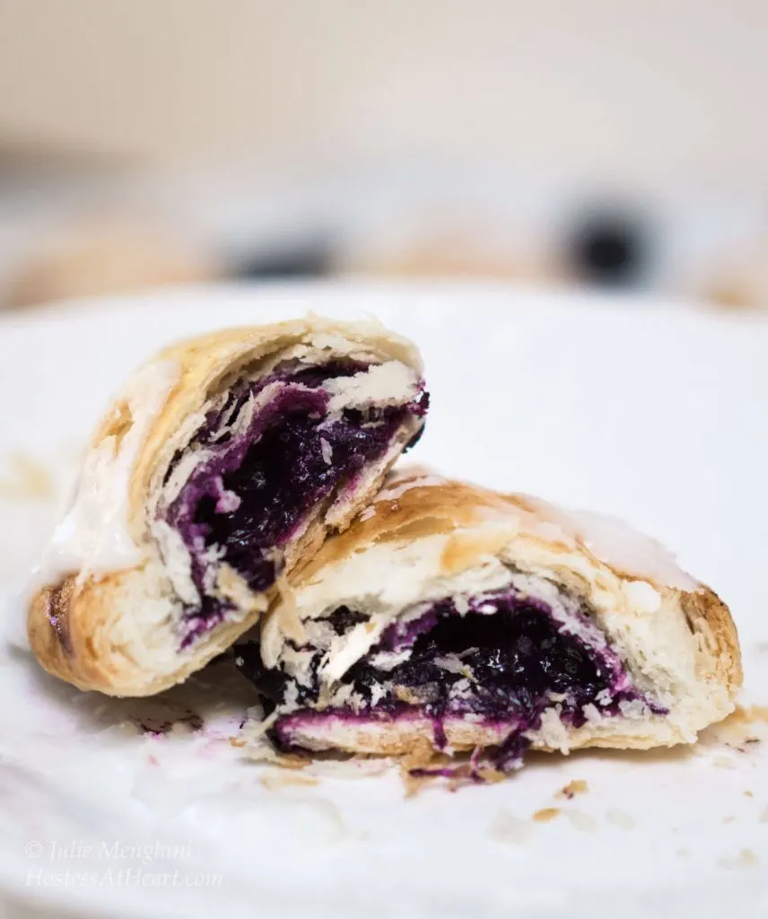 A blueberry pineapple hand pie cut in half showing the blue-purple filling sitting on a white plate.