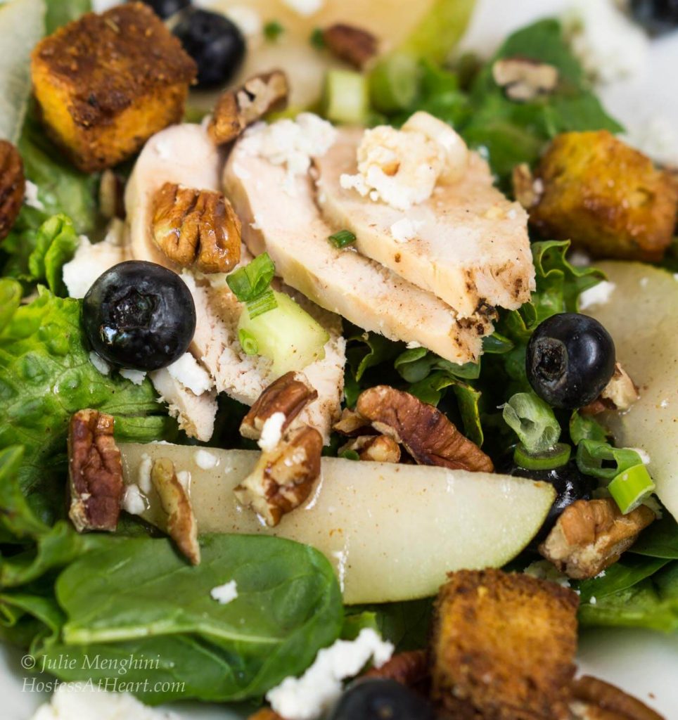 Green lettuce salad topped with sliced chicken, fresh pears, candied pecans, green onions, blueberries, and blue cheese crumbles.