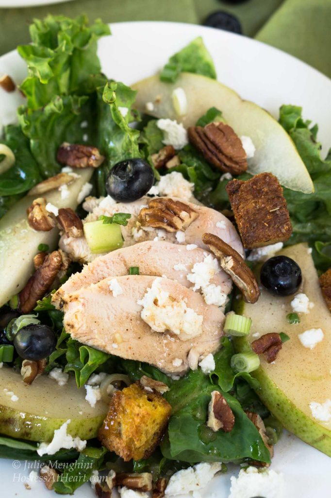 Green lettuce salad topped with sliced chicken, fresh pears, candied pecans, green onions, blueberries, and blue cheese crumbles.