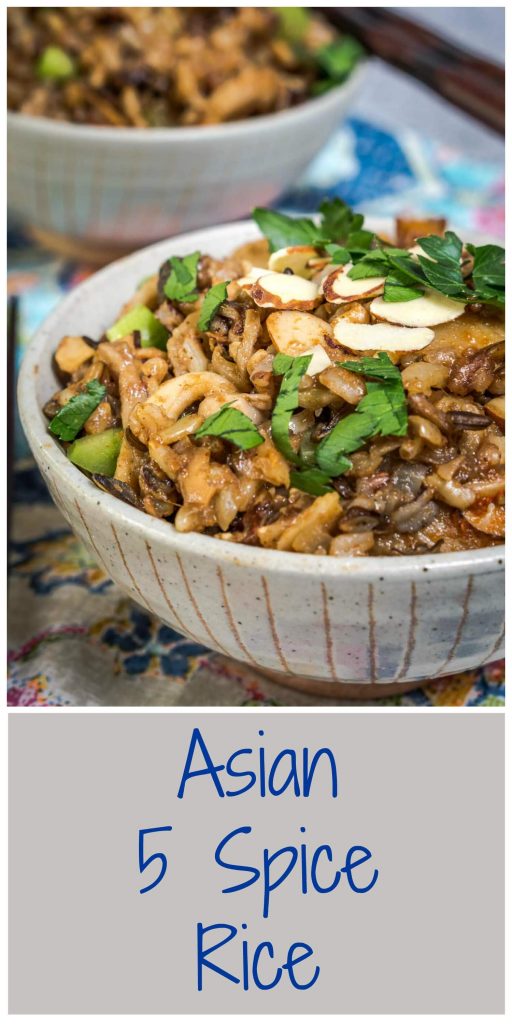 A front view of a gray bowl filled with 5 Spice Rice garnished with sliced almonds, sliced green onions, and chopped parsley. A second bowl sits in the background and a pair of chopsticks sit to the side over a colorful napkin. The title of the recipe \"Asian 5 Spice Rice runs beneath the photo.