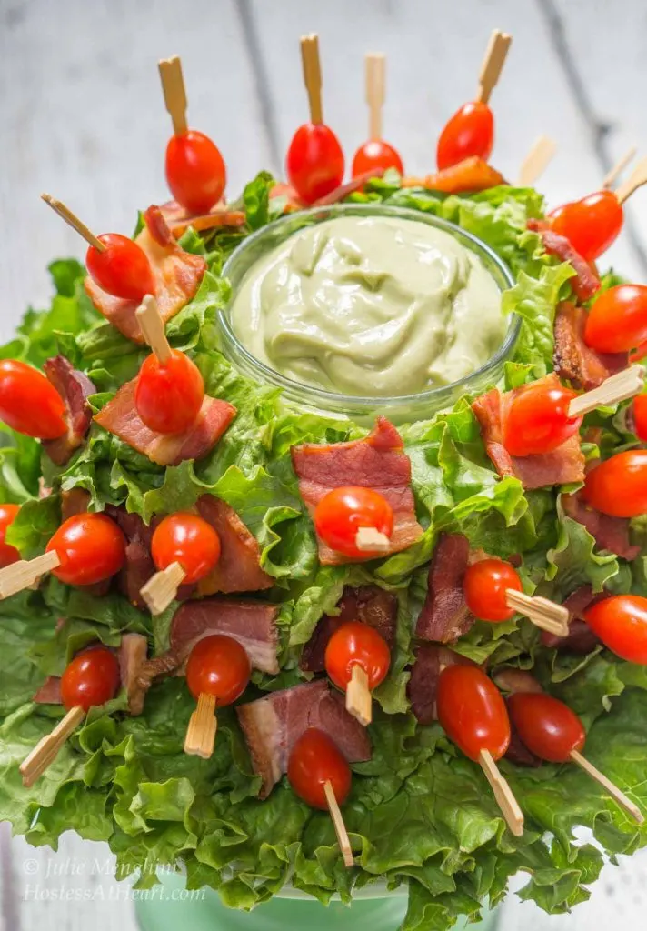 A head of lettuce with the top hollowed out which holds a small bowl of avocado sauce. Skewers hold pieces of lettuce, bacon and tomato adhering to the head of lettuce.