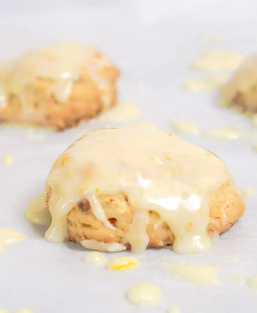 A side view of a Citrus Carrot cookies glazed in a citrus glaze sitting on white parchment paper.