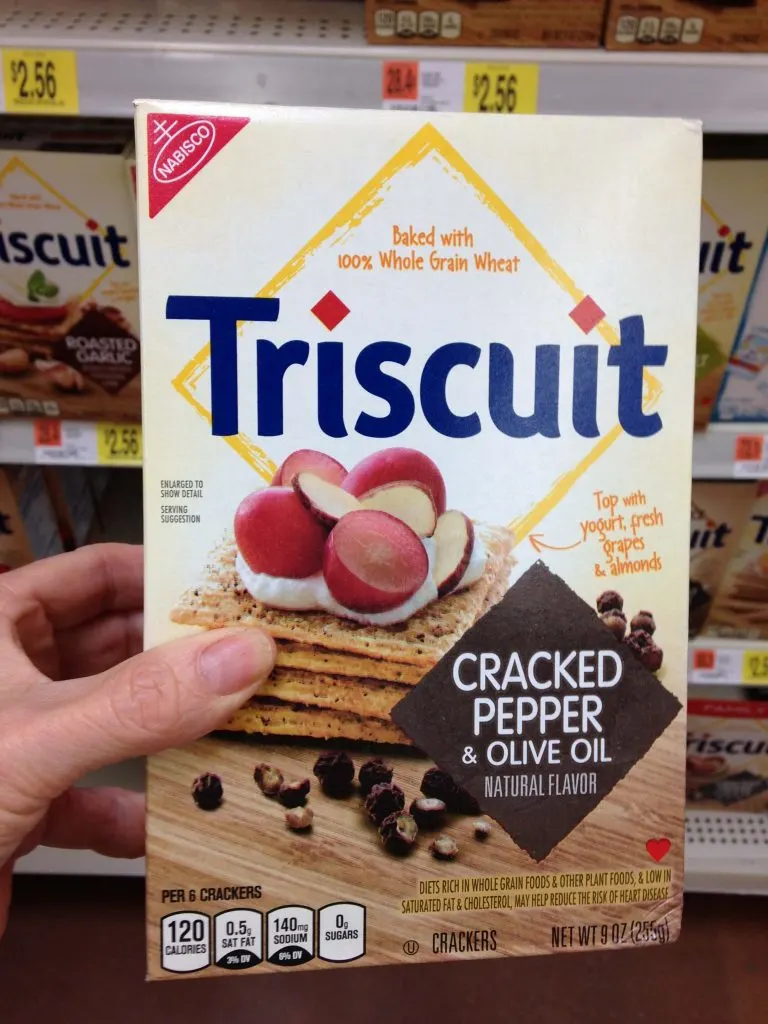 A hand holding a box of Cracked Pepper & Olive Oil Triscuit crackers.