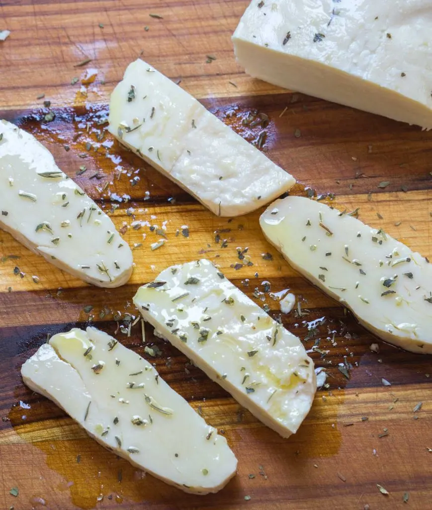 Slices of Halloumi cheese drizzled with olive oil and herbs sit on a wooden cutting board.