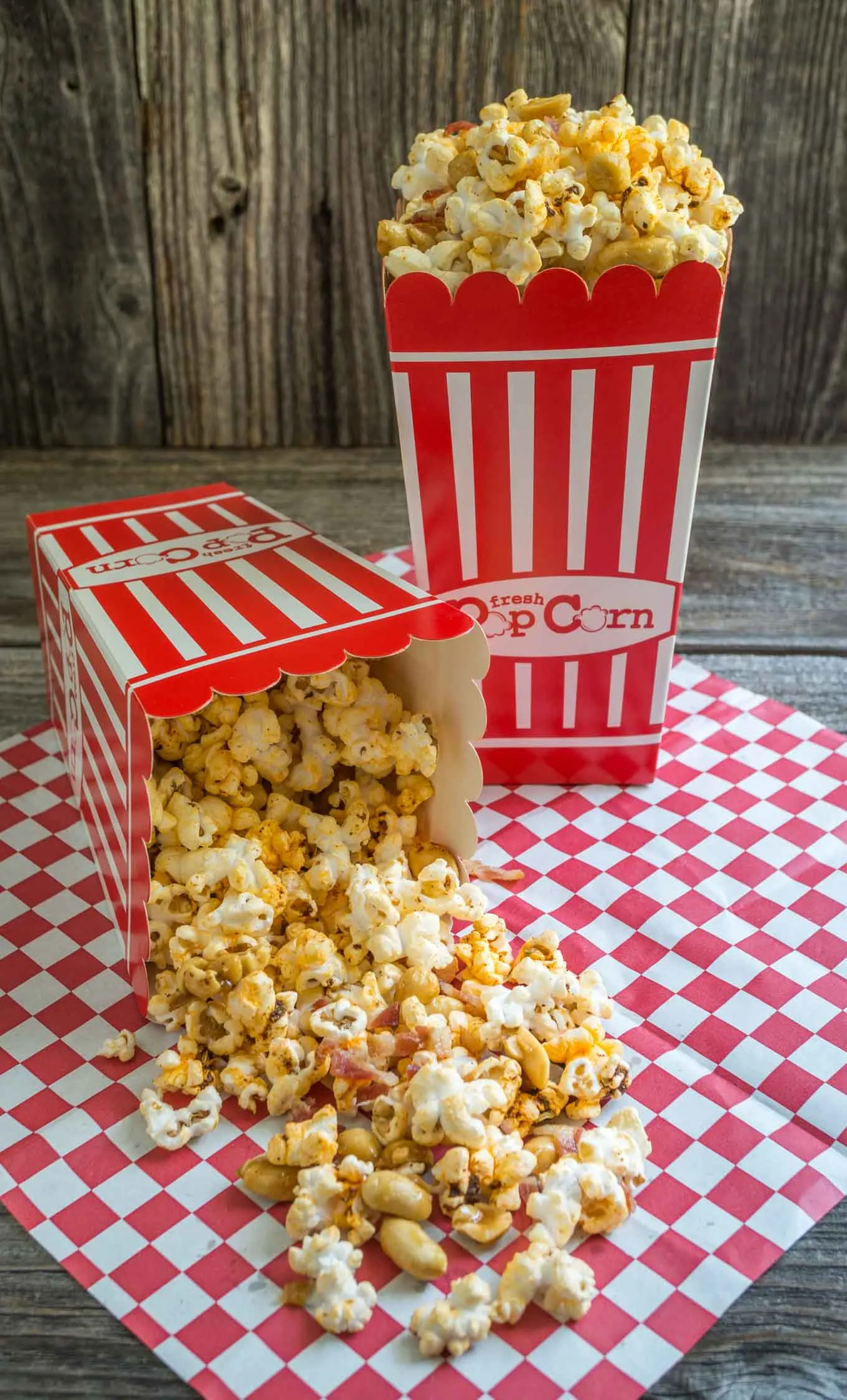 Popcorn box tipped over spilling Honey Nut Popcorn with bacon onto a red checked paper napkin. An upright box sits in the background,