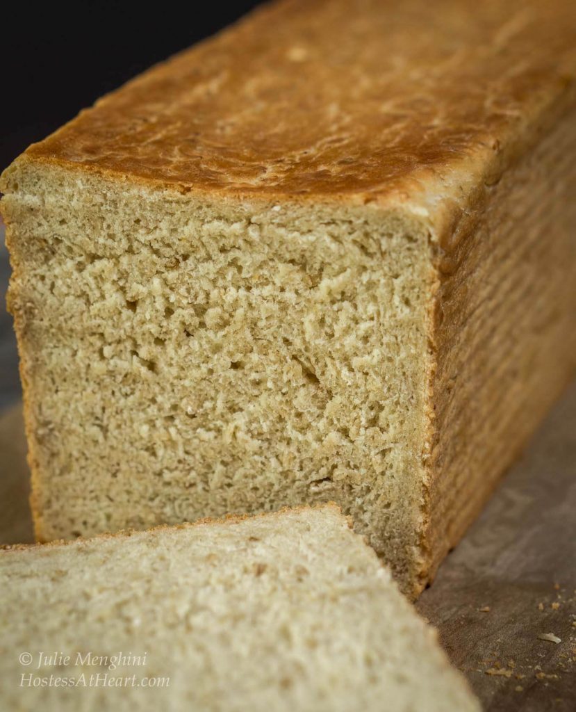 Front table-view of a loaf of Honey Oat Pain de Mie bread with one slice cut from the front showing a soft crumb and a toasted crust.