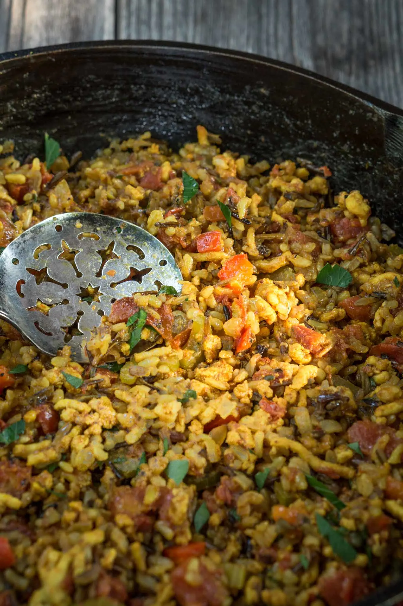 A cast-iron pan filled with Turmeric Chicken and rice with an antique serving spoon in the center.