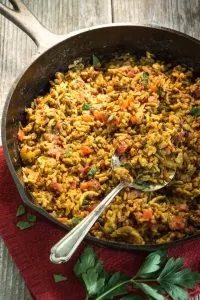 A cast-iron skillet filled with Chicken a Wild Rice. A serving spoon sits on the side.