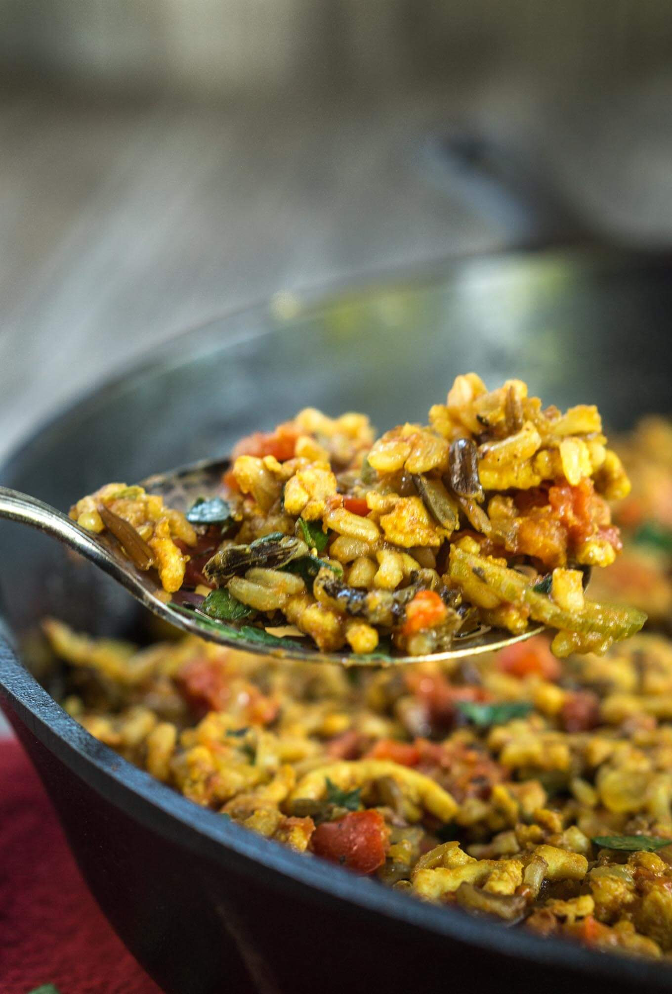 A spoonful of Turmeric Chicken and rice hovers over a black bowl filled with the dish.