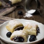 The blueberry puff pastry rolls on a white plate with the title of the recipe printed on top of the photo