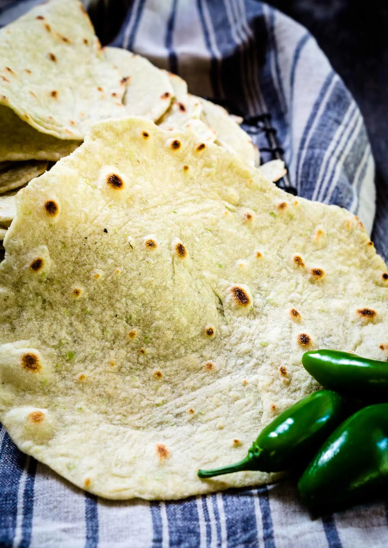 A close up of a fresh tortilla with fresh jalapenos sitting in the foreground.
