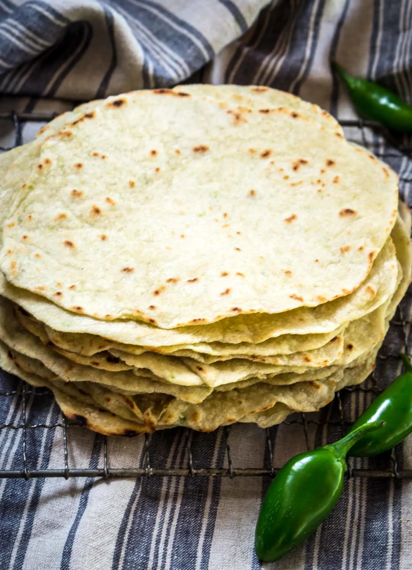 A stack of homemade tortilla shells on a cooling rack. Fresh jalapenos sit in the front and back.