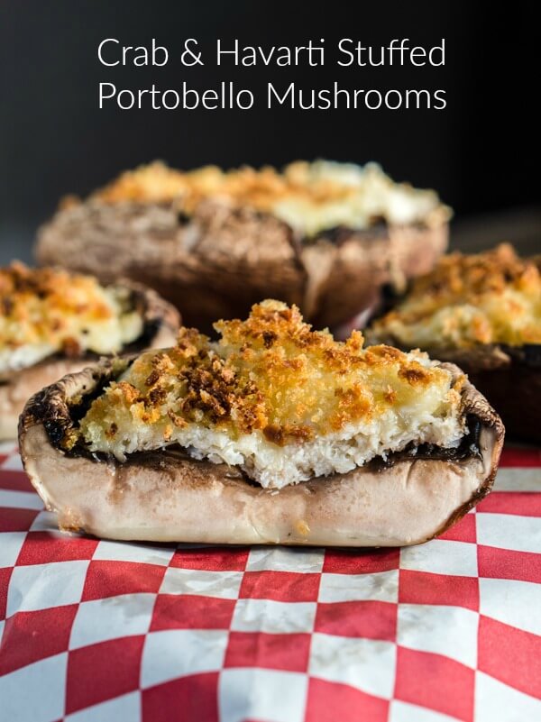 A side view of a portobello mushroom that is stuffed with crab and topped with toasted breadcrumbs sitting on a red checked napkin. Stuffed mushrooms sit in the background.