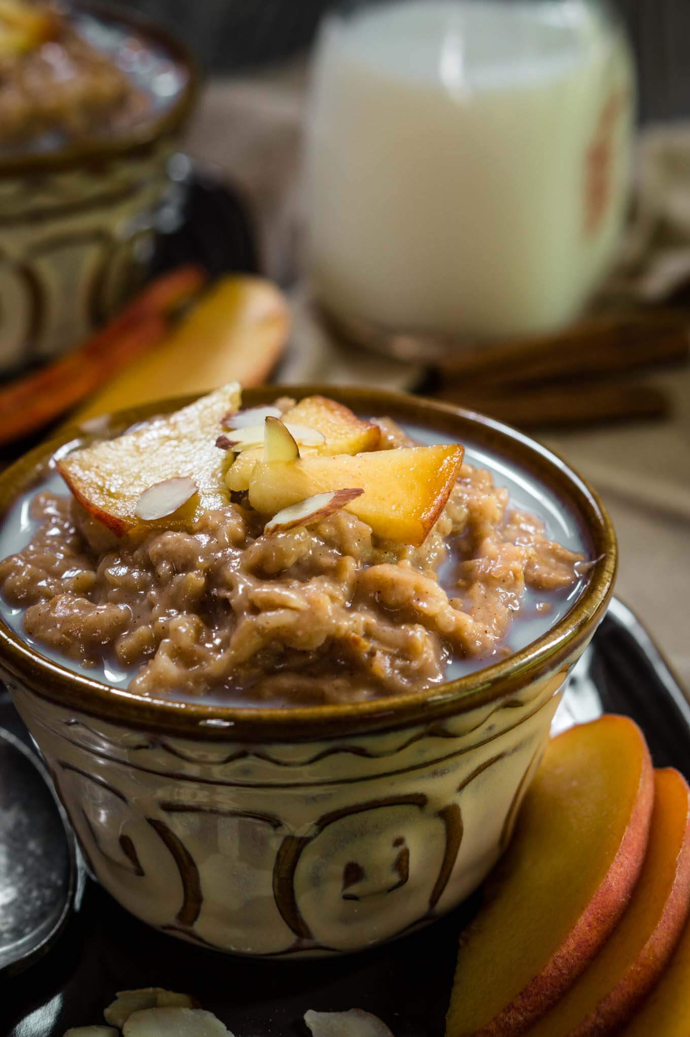 A yellow dish filled with Steel-cut Oats and Bulgar that\'s topped with warm milk, cinnamon, fresh peaches, and nuts. Fresh sliced peaches sit to the side. A jar of milk and a second dish sits in the background.