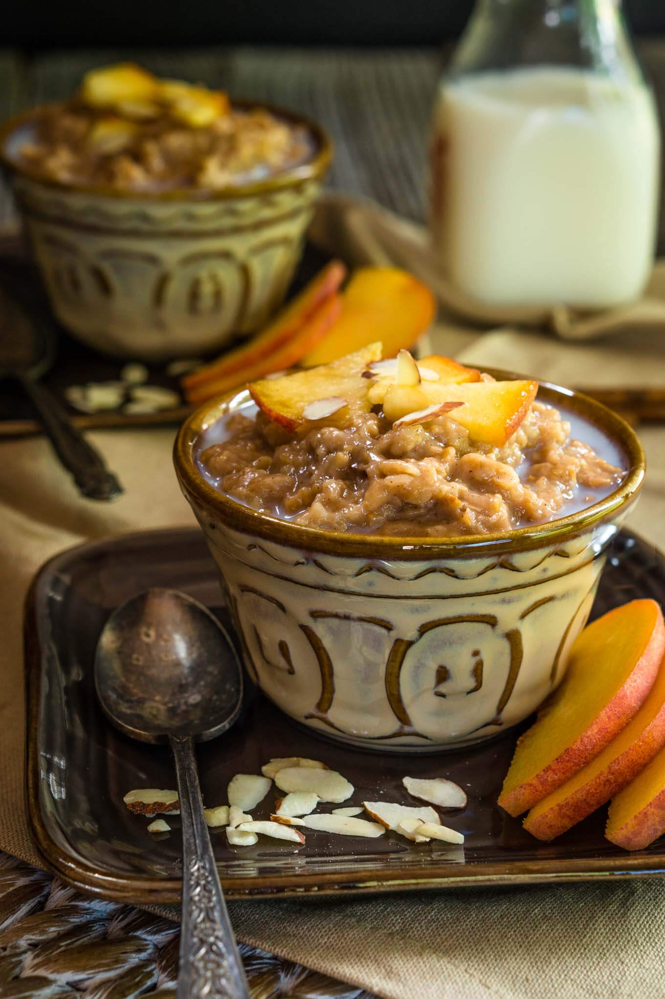 A yellow dish filled with Steel-cut Oats and Bulgar that\'s topped with warm milk, cinnamon, fresh peaches, and nuts. Fresh sliced peaches sit to the side. A jar of milk and a second dish sits in the background.