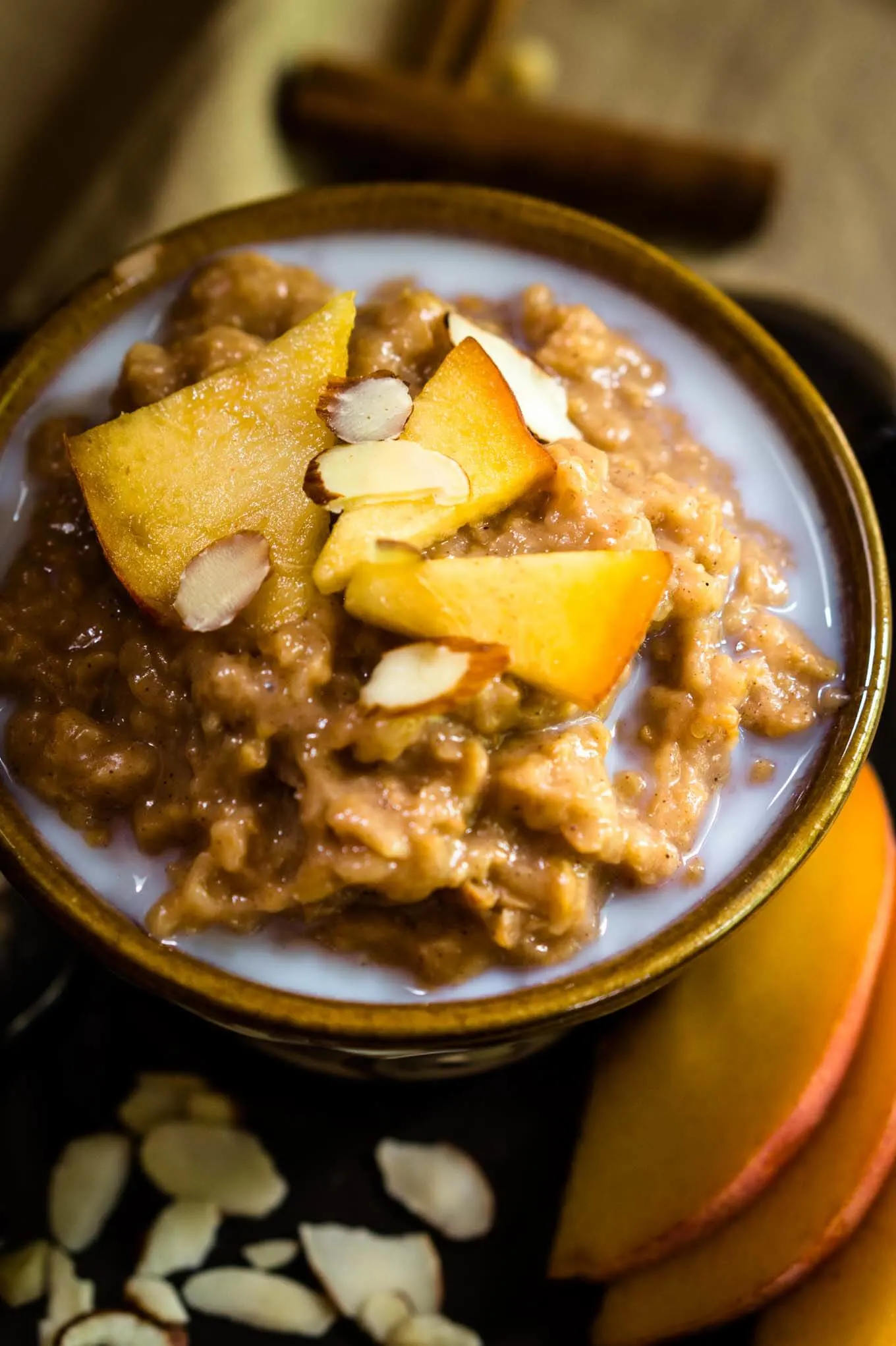 Top-down view of a yellow dish filled with Steel-cut Oats and Bulgar that\'s topped with warm milk, cinnamon, fresh peaches, and nuts. Fresh sliced peaches sit to the side. 