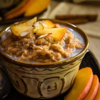 A yellow dish filled with Steel-cut Oats and Bulgar that's topped with warm milk, cinnamon, fresh peaches, and nuts. Fresh sliced peaches sit to the side.