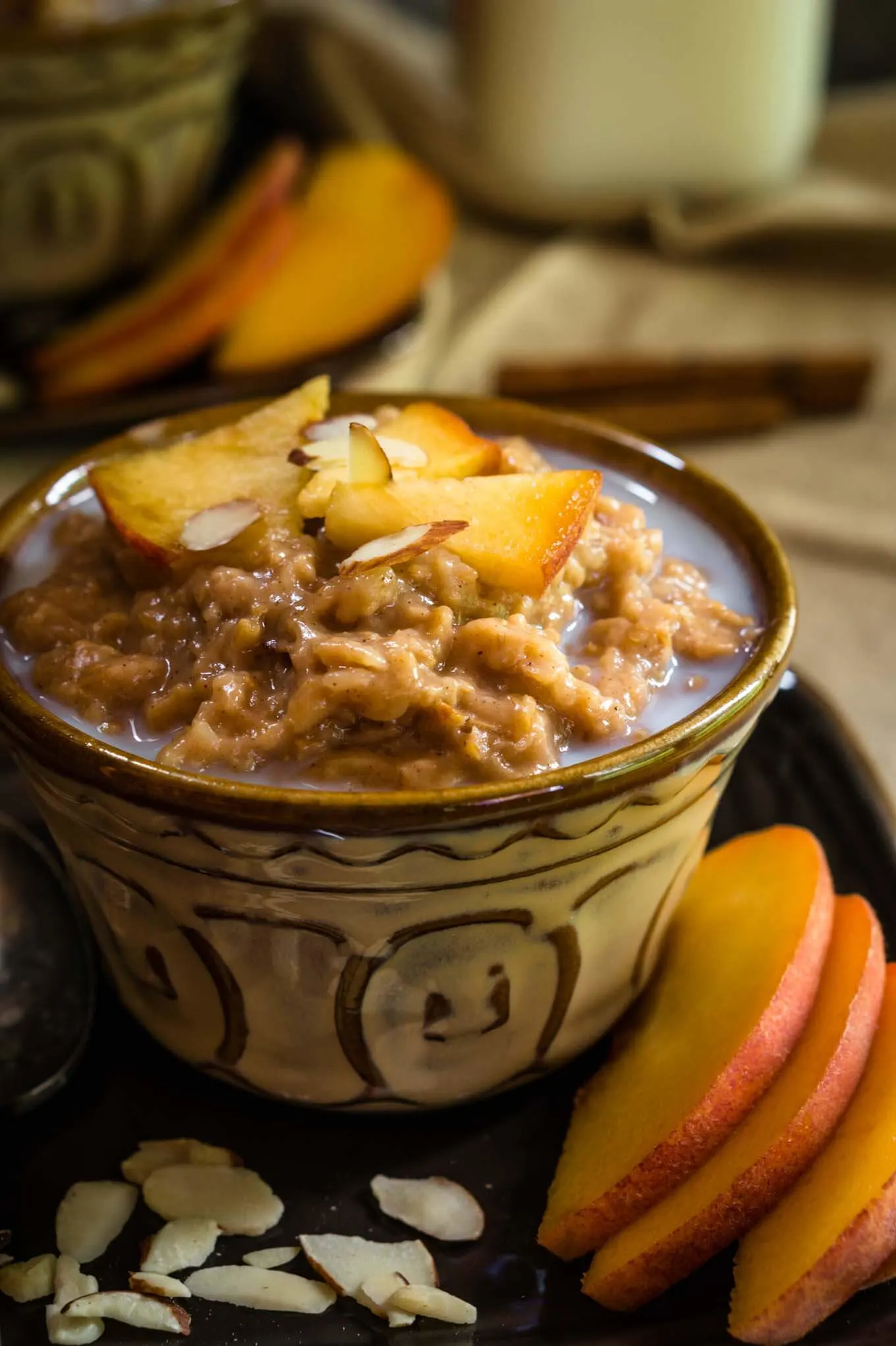 A yellow dish filled with Steel-cut Oats and Bulgar that's topped with warm milk, cinnamon, fresh peaches, and nuts. Fresh sliced peaches sit to the side.