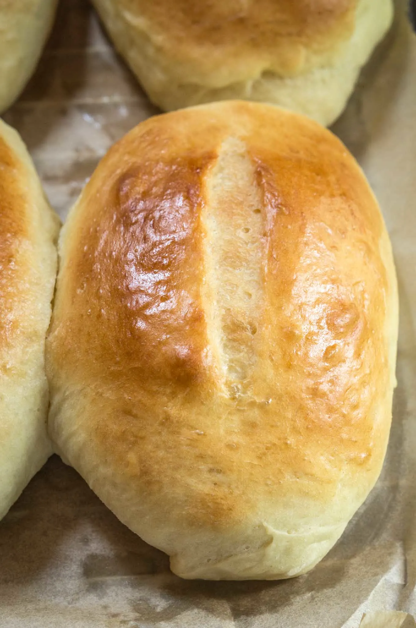 Top view of a golden brown Medianoche roll sitting on a cooling rack over parchment paper.