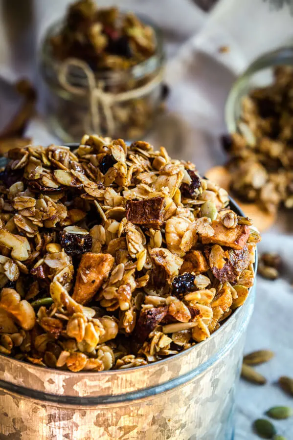 A tin filled with granola made with dried fruit sits in front of two small jars full of the granola.