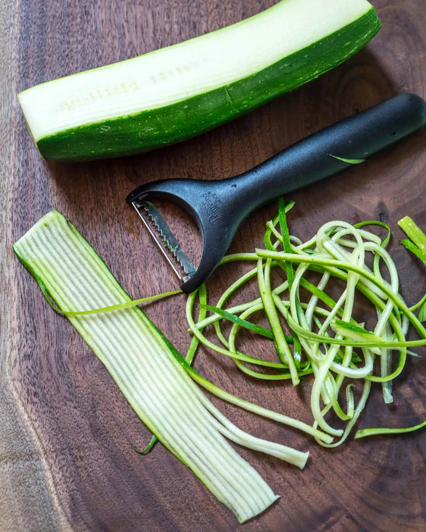  A wooden board topped with sliced zucchini and julienned strips next to the Julien tool.