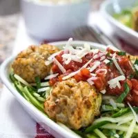 A white bowl of spiralized zucchini topped with chicken meatballs and marinara.