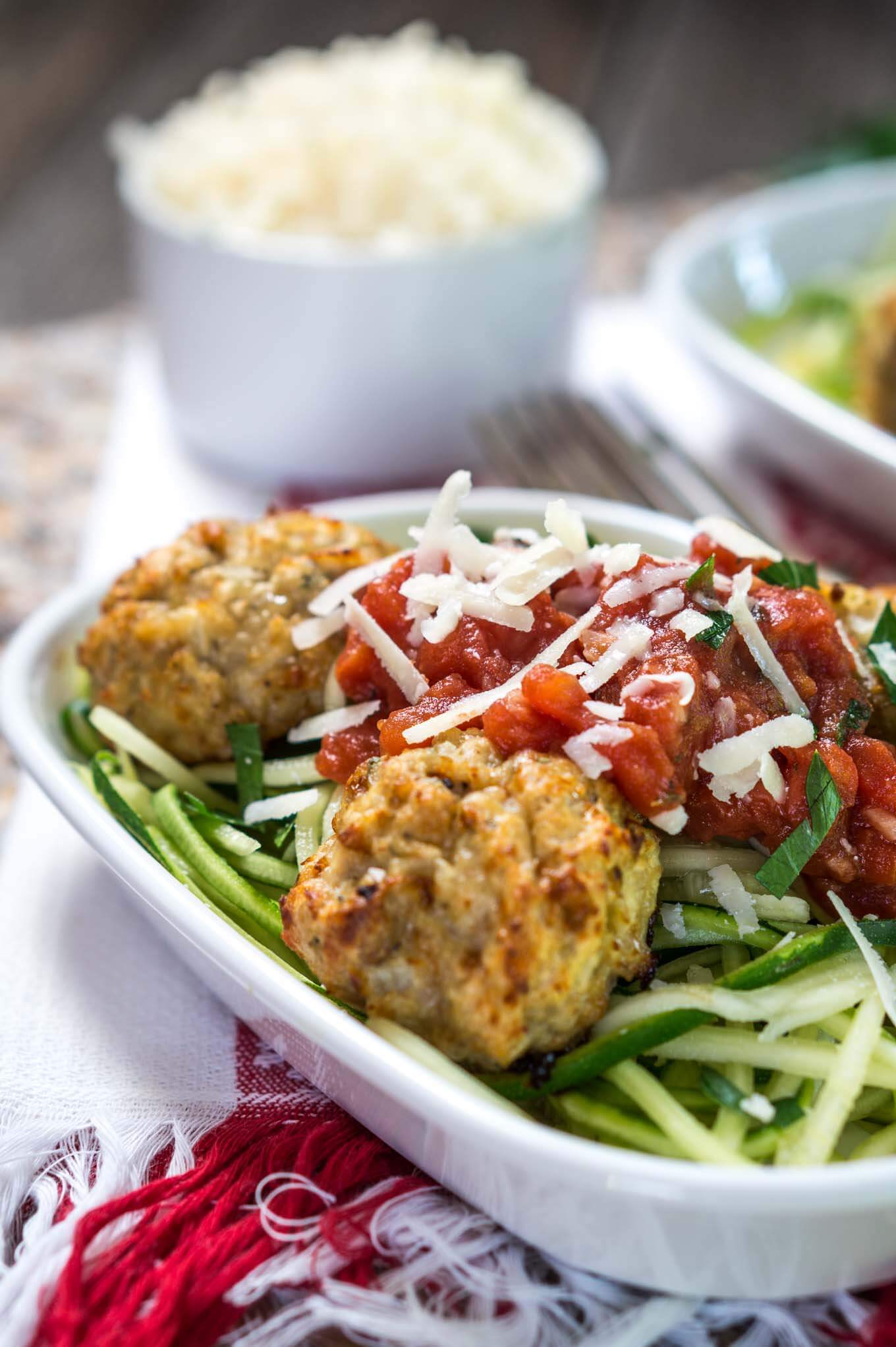 A white bowl of spiralized zucchini topped with chicken meatballs and marinara.