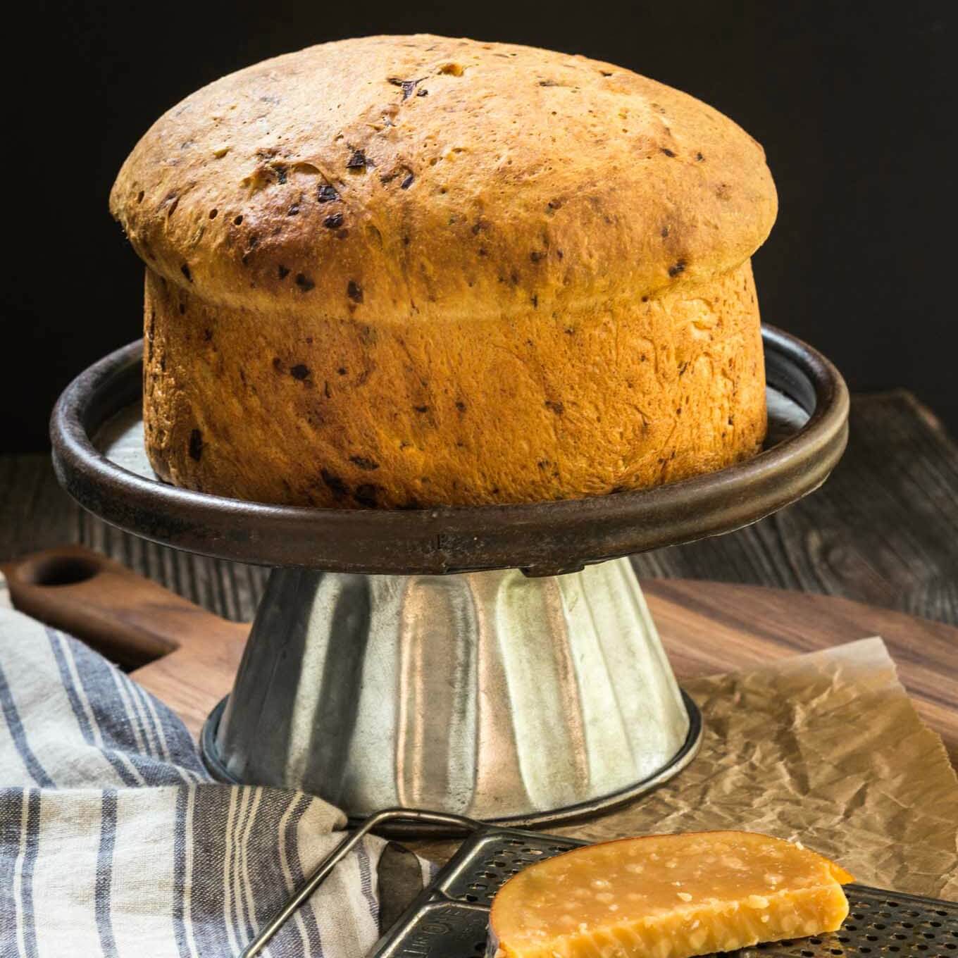 A loaf of Onion Gouda bread sitting on a cake stand over a blue striped napkin.