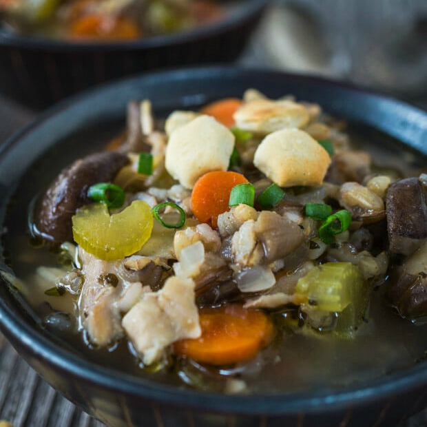 A black bowl filled with Chicken and Rice soup that\'s full of carrots and celery. A second bowl sits in the background.