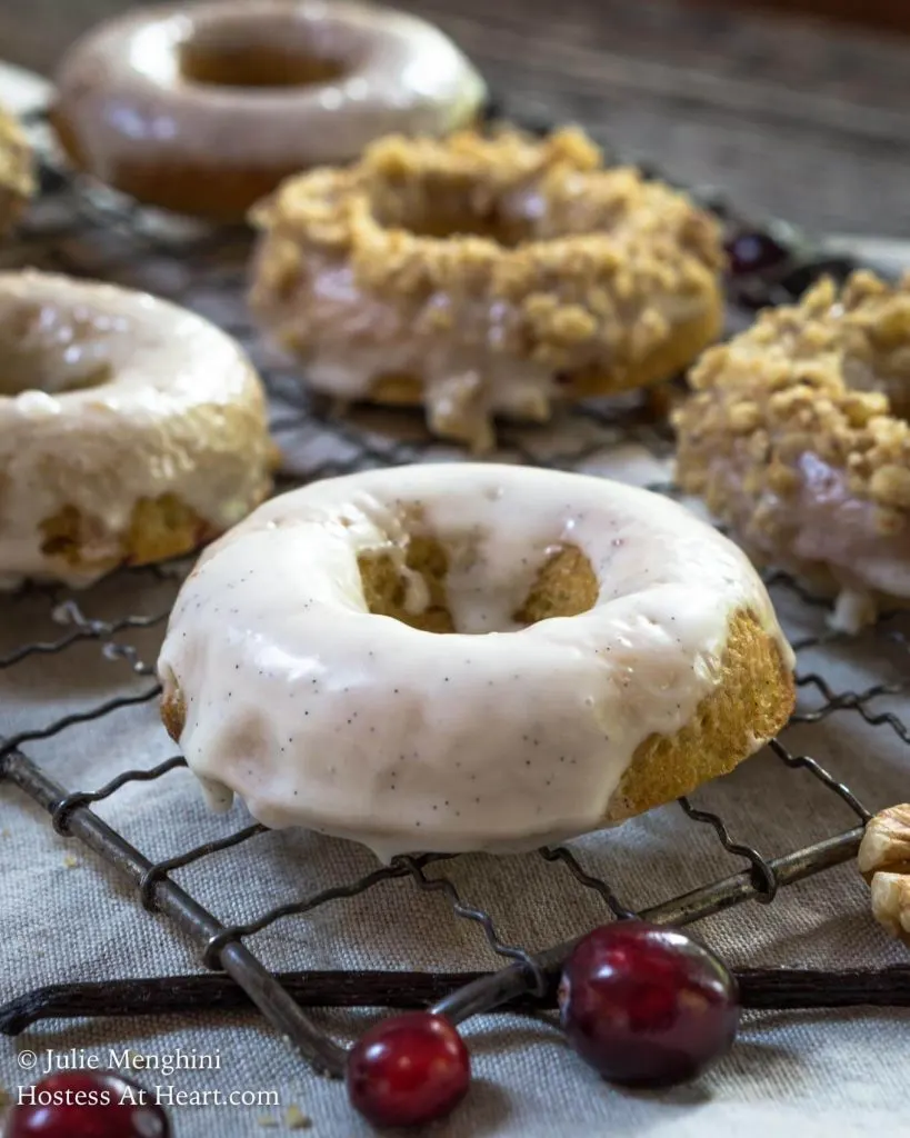 Side shot of a rack showing iced donuts with some topped with chopped nuts. HostessAtHeart.com