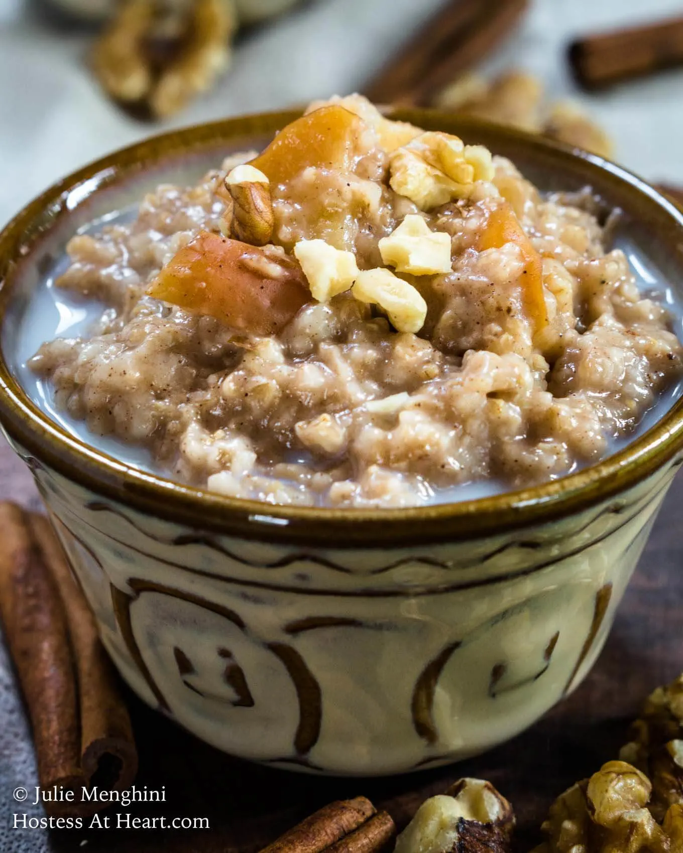 Close-up view of a bowl of Spiced Apple Steel Cut Oats sitting on a wooden cutting board. The bowl is sprinkled with nuts and raw apples. 