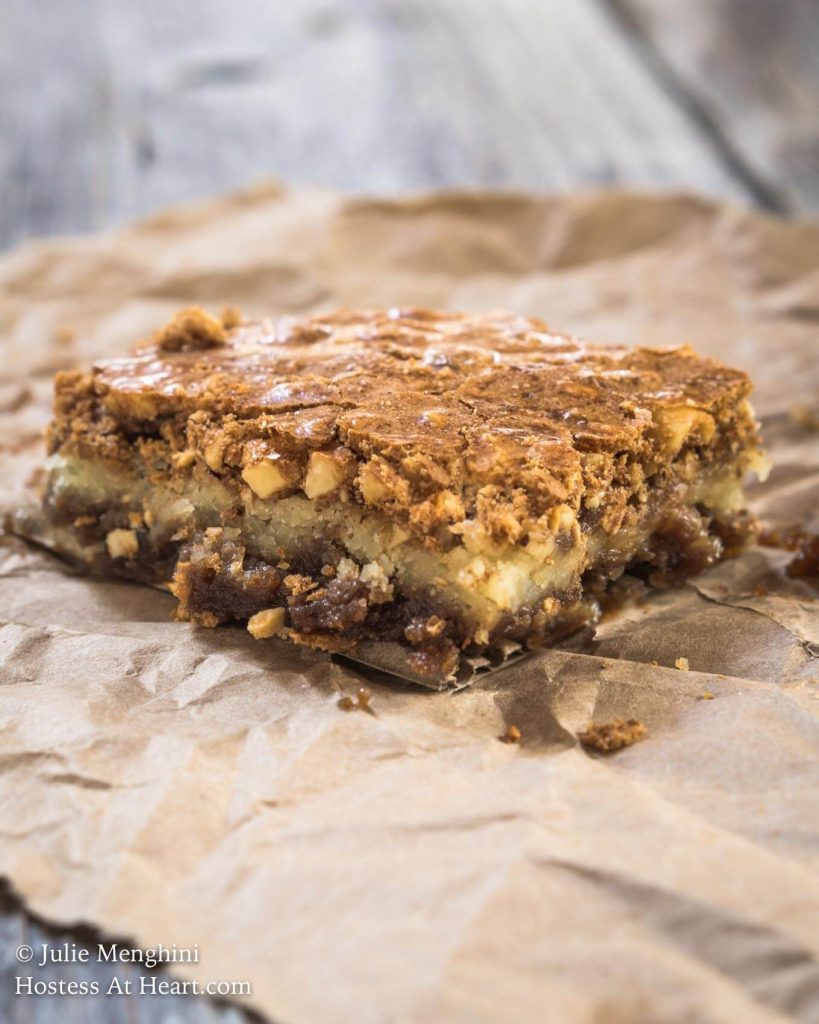 A side view of a hazelnut cookie bar sitting on parchment paper over a wooden background.