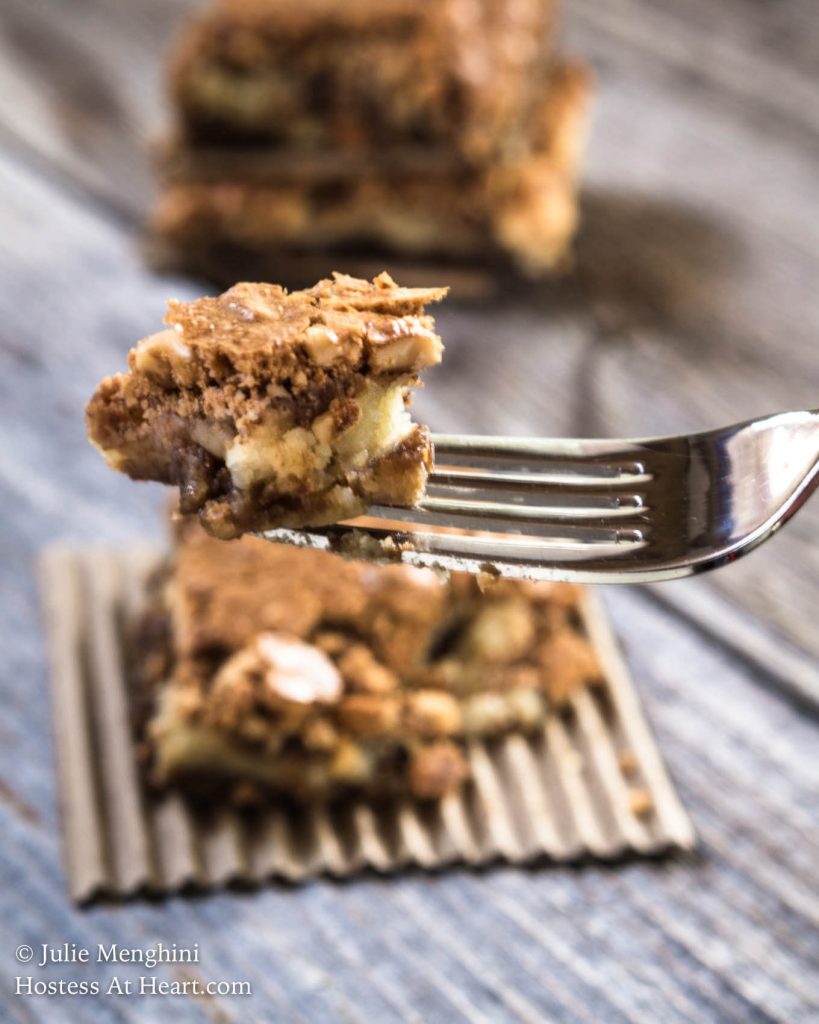 A forkful of a hazelnut cookie bar hovering over a hazelnut cookie bar sitting on a piece or corrugated cardboard.