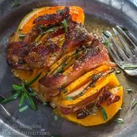 A butternut squash sliced with bacon interwoven topped with rosemary