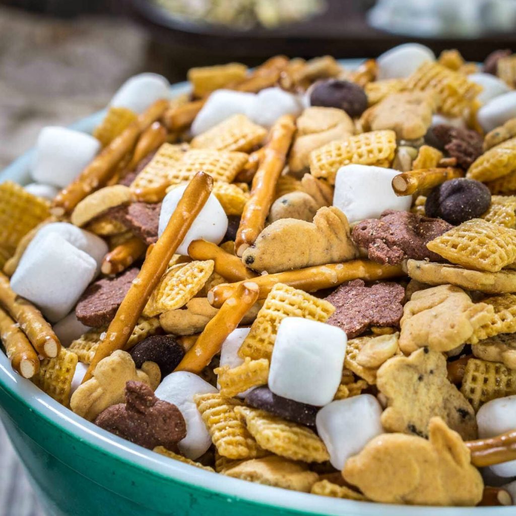 A green bowl of snack mix made with graham cracker bunnies, cereal, marshmallows, pretzels, and chocolate chips.