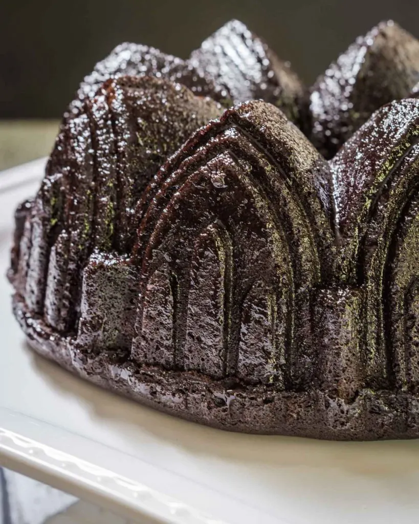 A Raspberry Chocolate Pound Cake baked in a bundt pan and drizzled with a Raspberry Glaze sitting on a white platter.