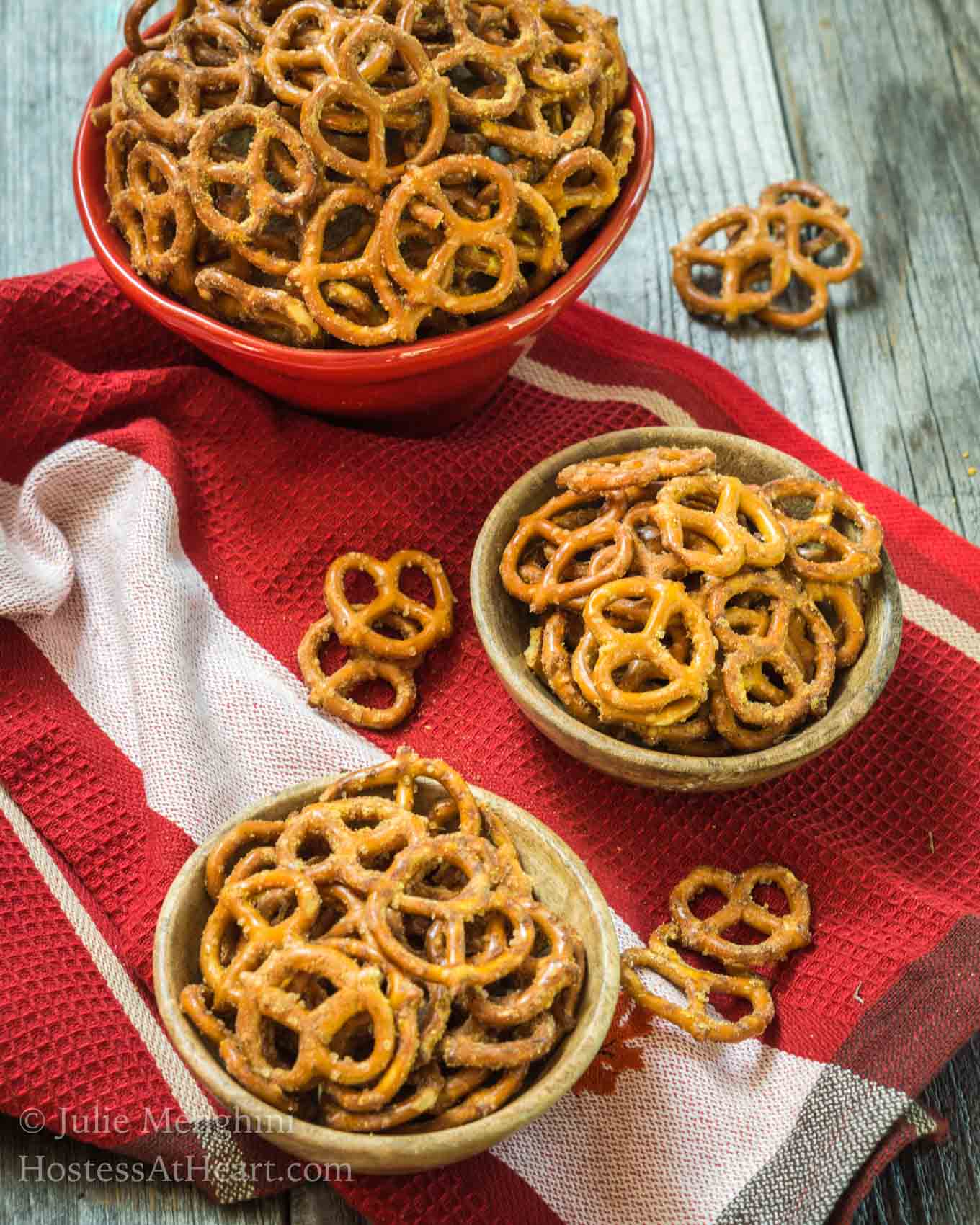 Top-down view of two small wooden bowls and one red bowl filled with pretzels that have been baked in a spicy Nacho Cheese seasoning. Pretzels have been scattered about the bowls.